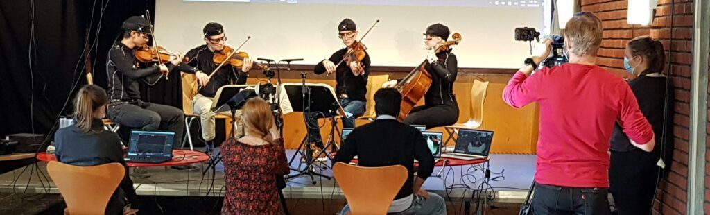 Musicians on stage with many different types of sensors on, with RITMO researchers running the data collection and a team from LINK filming.